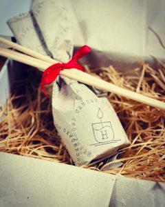 A wrapped diffuser bottle tied with a red ribbon and laying on a bed of straw in a white gift box
