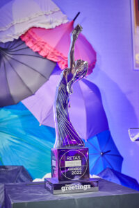 Picture of a silver award statue against a vibrant background of purple and pink umbrellas