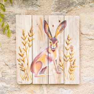 A hand-painted illustration by Liz Corley Art of a hare in a field of wheat painted on wood