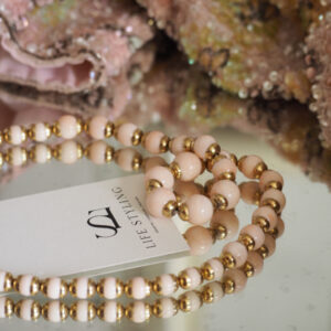 A pink and gold beaded necklace on a glass cabinet surrounding a business card for Life Styling, a vintage clothing brand.