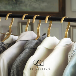 A rail of cream, beige and grey clothing on brass coloured coat hangers. The branding of intertwined letters L and S for Life Styling appears bottom centre.
